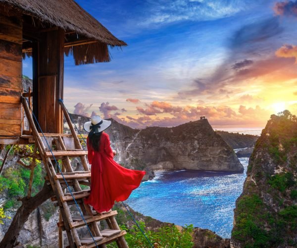 Young girl on steps of house on tree at sunrise in Nusa Penida island, Bali in Indonesia.